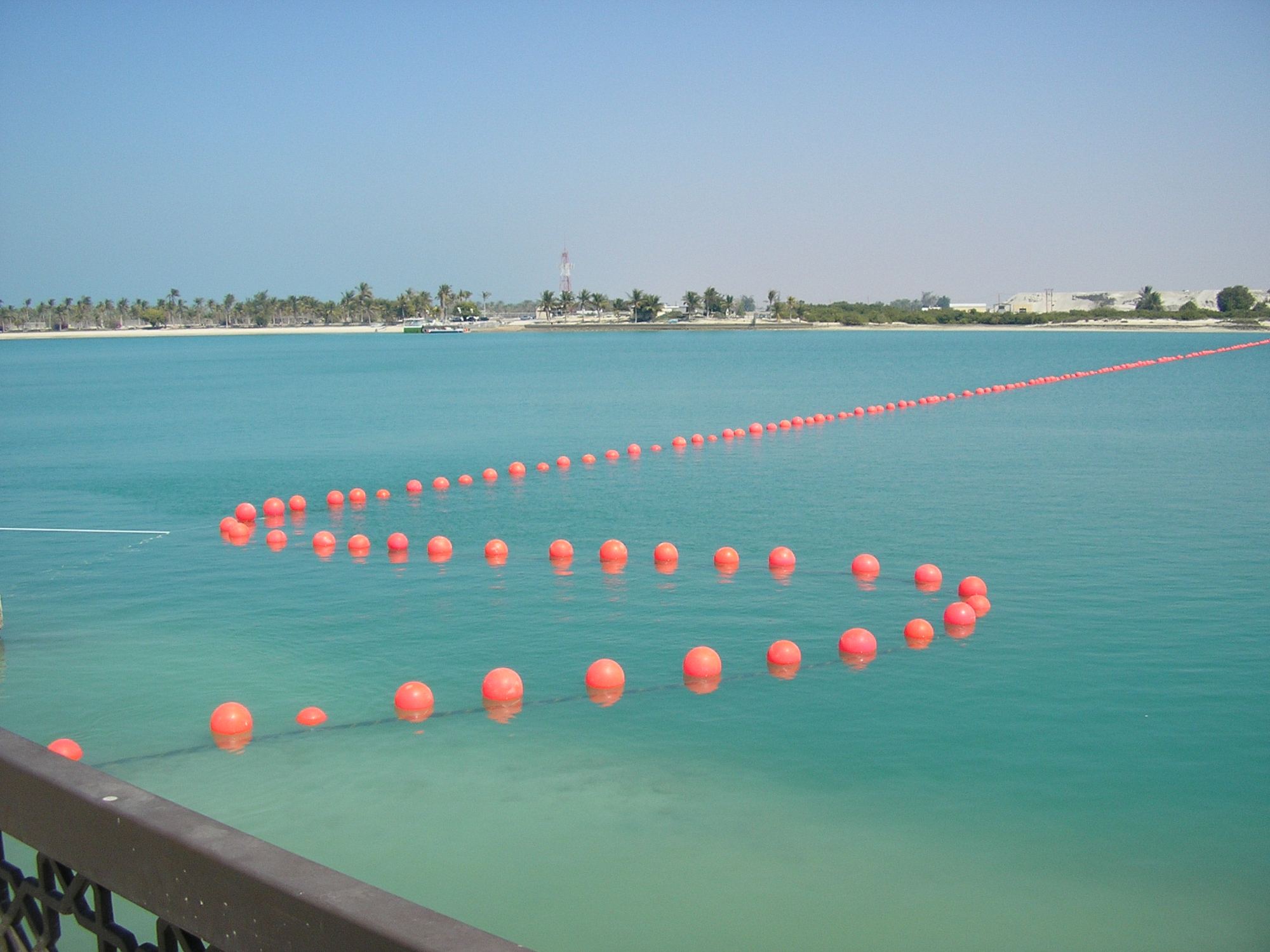 A submarine cable floated on a line of orange buoys across shallow turquoise water before being lowered to the seabed